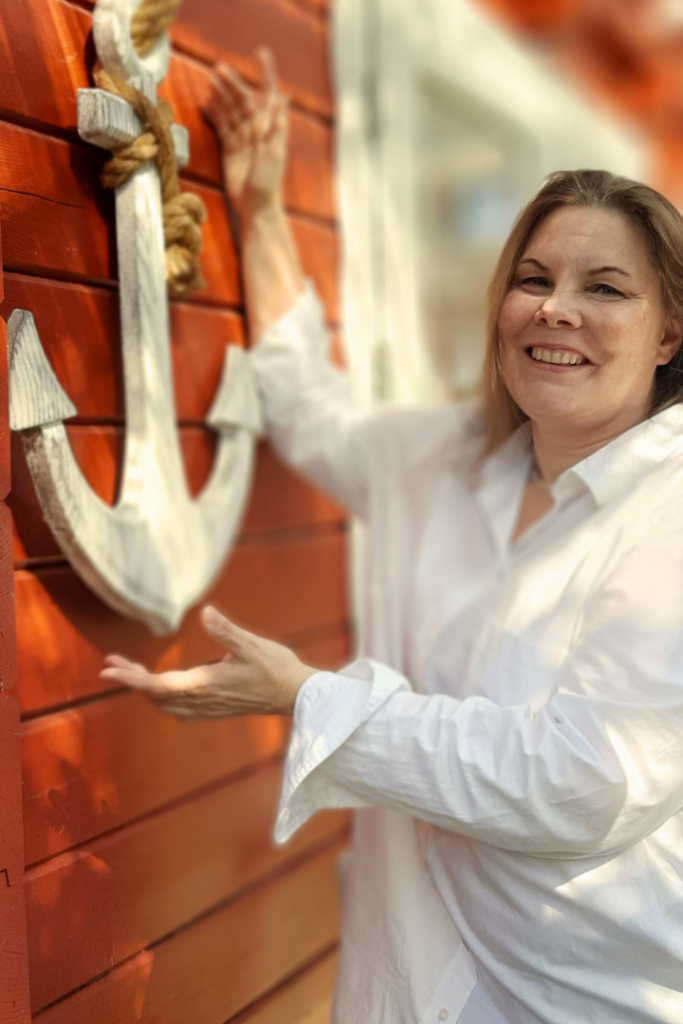 Viola Ehlers steht an ihrer Praxis und hält einen Anker in der Hand. Sie bietet Stressmanagement bei Hamburg an.